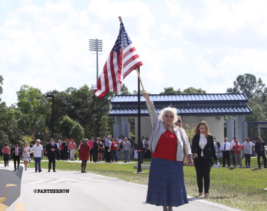 A woman waves an American flag near the Ocean Bank Convocation Center on Monday, Feb. 18. Behind her is a line of Trump supporters waiting to enter the arena.